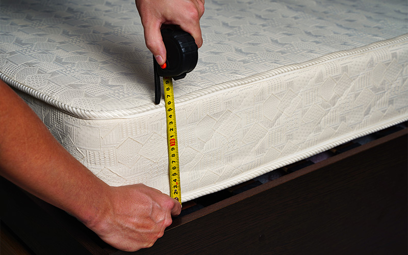 A person using a yellow tape measure to check the thickness of a single mattress.