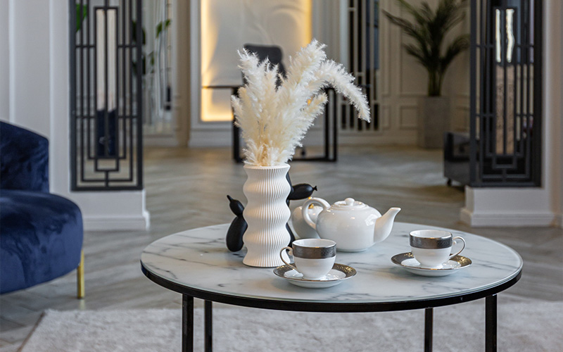 A stylish marble coffee table set with a white teapot and silver-rimmed tea cups