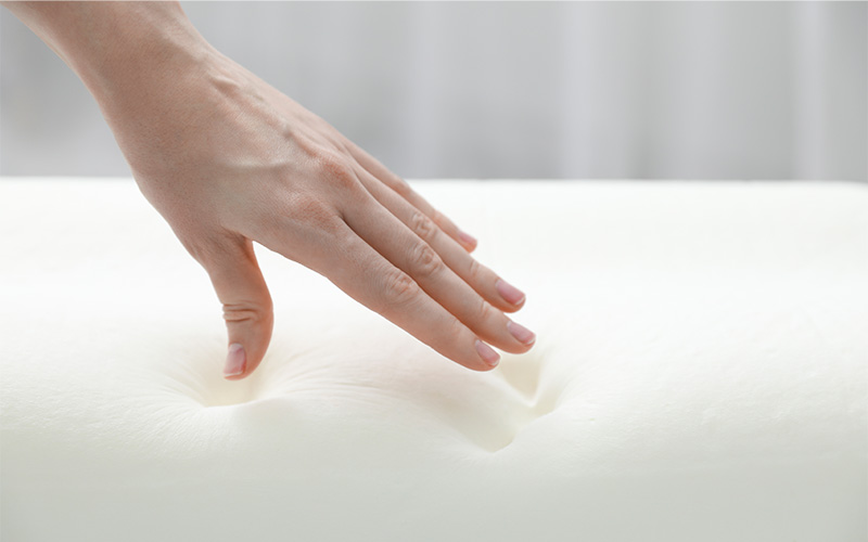 Hand presses into soft white memory foam surface.