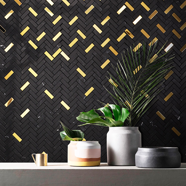 Black and gold herringbone mosaic tiles on the wall behind a vase