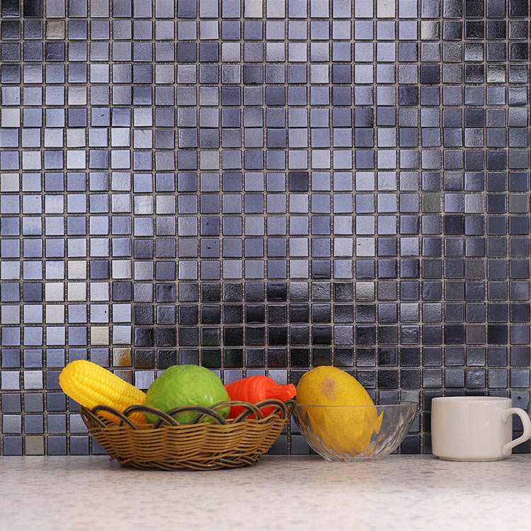 Black metallic glass mosaic tiles on the wall with some fruit and a white cup in front.