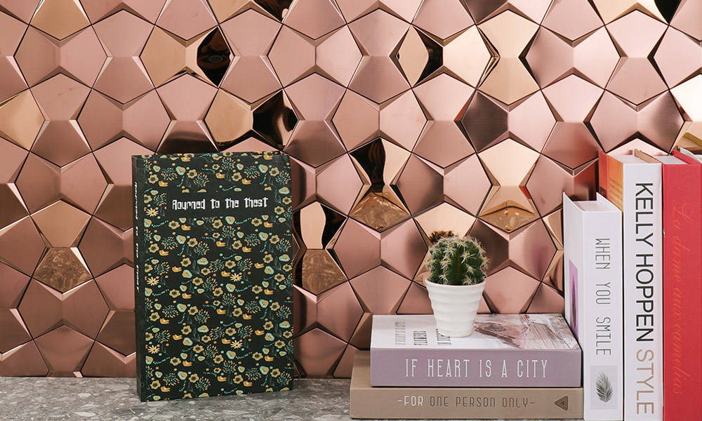 Rose gold 3D stone-shaped mosaic tiles on the wall with some books in front.