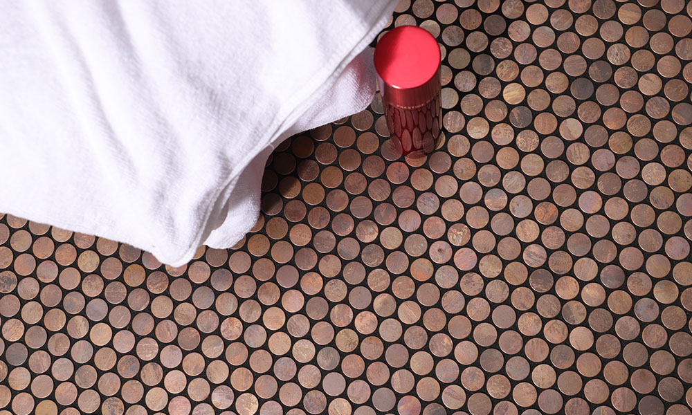 Copper penny round mosaic tile with black grout, white towel, and red shampoo bottle