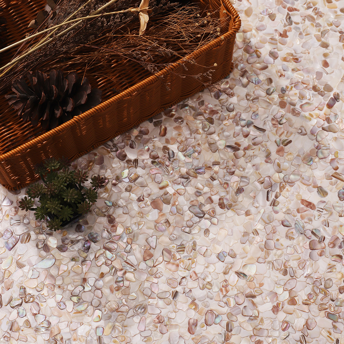 Mother of pearl shell fragments in pink and white with pinecones and plants around.