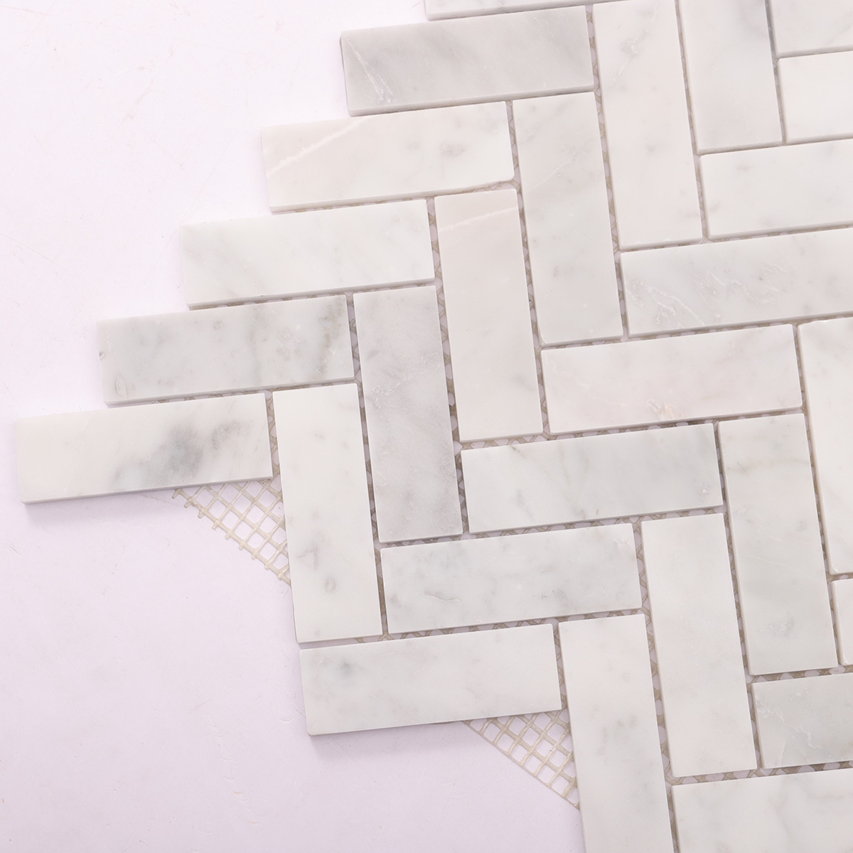 Detailed close-up of polished herringbone Carrara white marble mosaic tiles