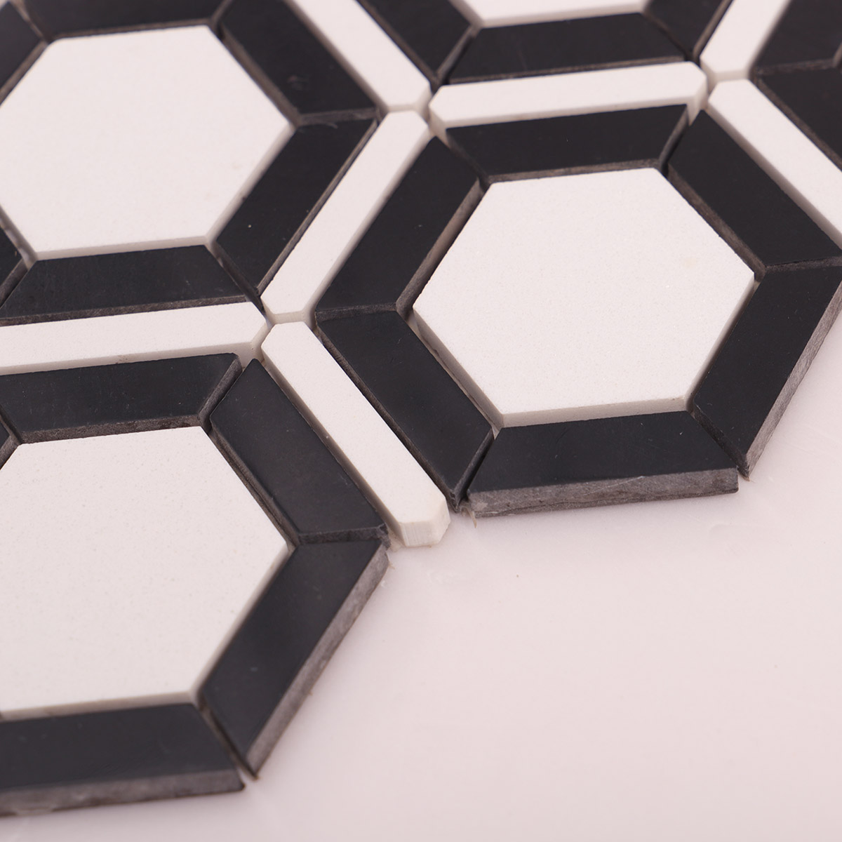 Side close-up view of white and black hexagon marble mosaic tiles, showing texture and thickness.