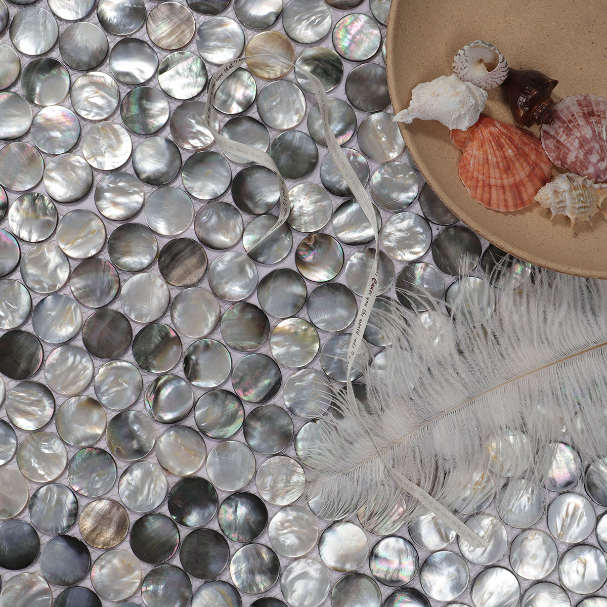 Close-up of black mother of pearl penny round tiles, with a white feather.