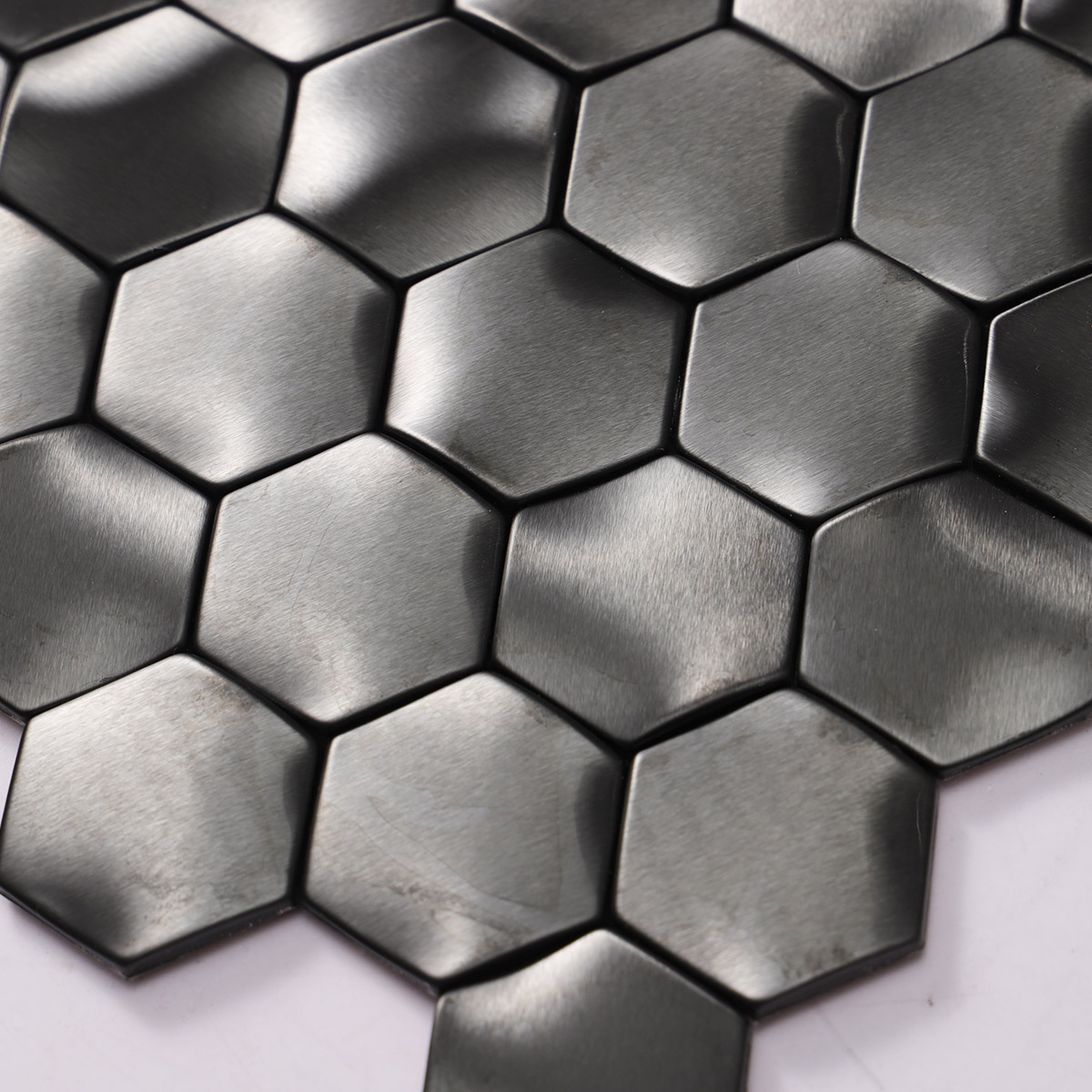 Close-up view of wavy 3D metal black brushed stainless steel hexagon mosaic tiles.