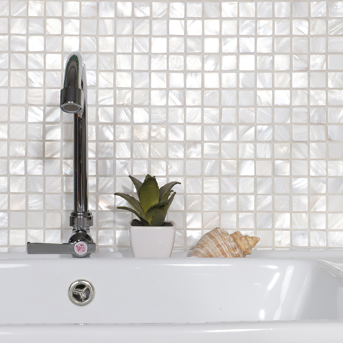 Bathroom wall with white mother of pearl square tiles and water faucet.