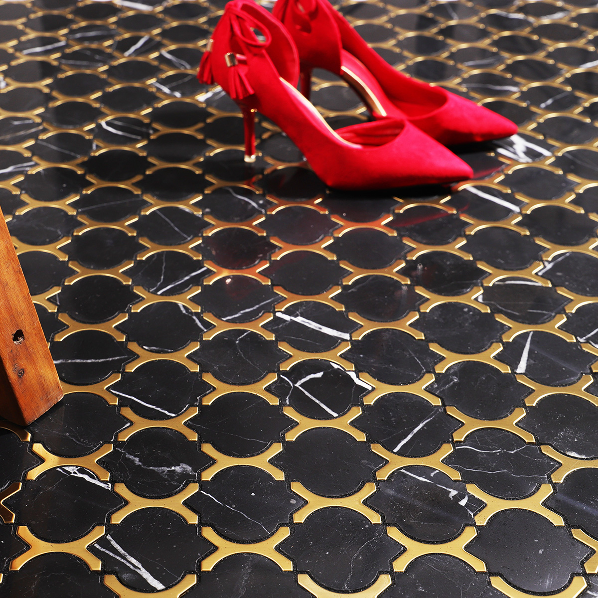 Black marble and gold stainless steel arabesque mosaic tiles on floor with red high heels.