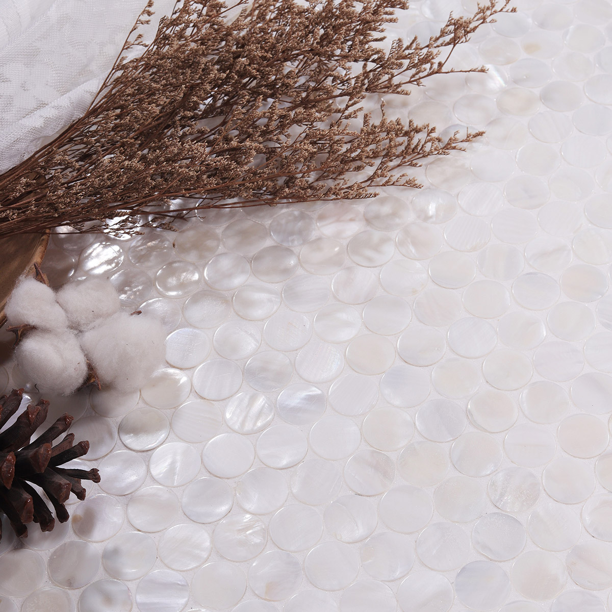 Close-up of penny round mother of pearl mosaic tiles with dried branches and gauze beside them.