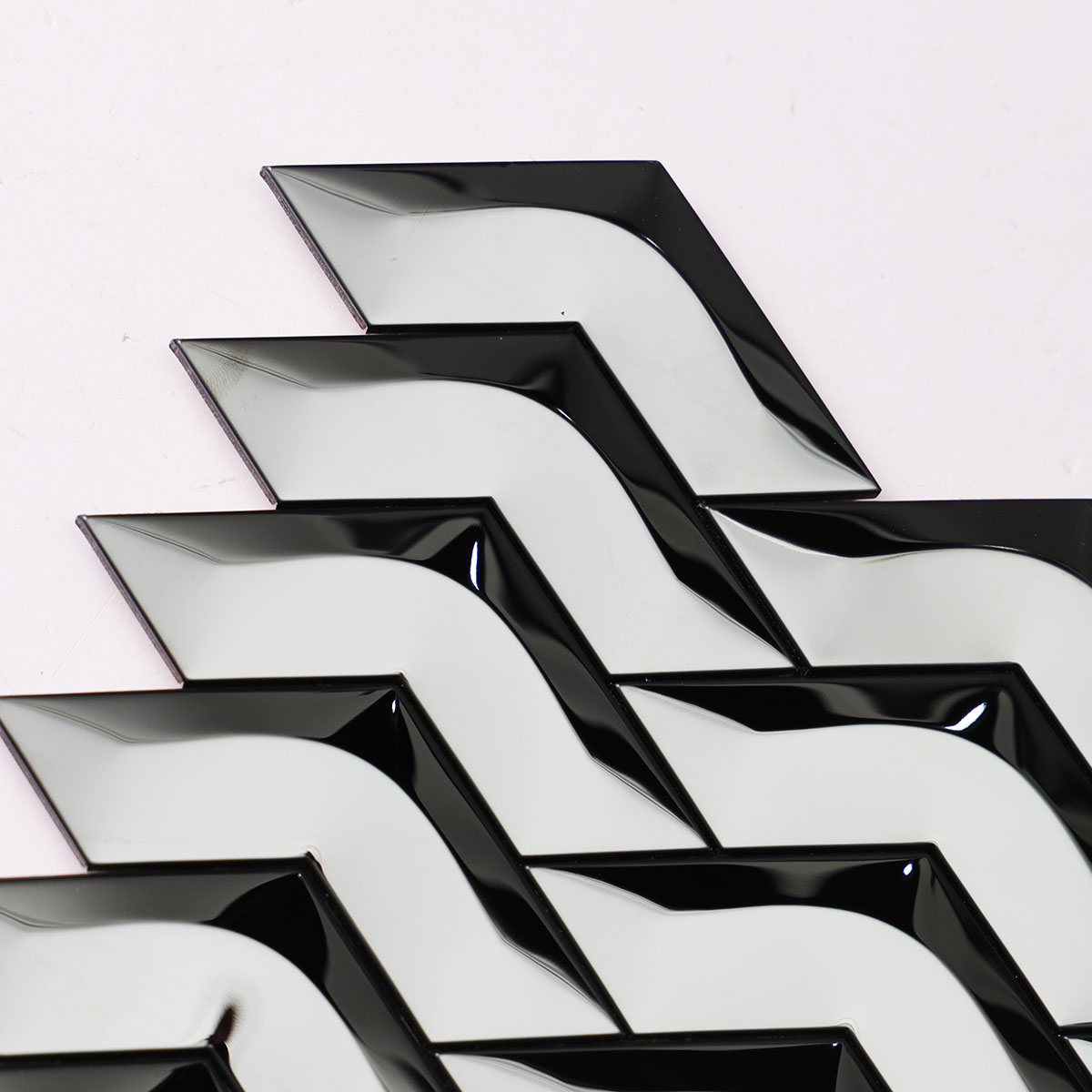 Macro close-up of black stainless steel chevron 3D mirror mosaic tiles.