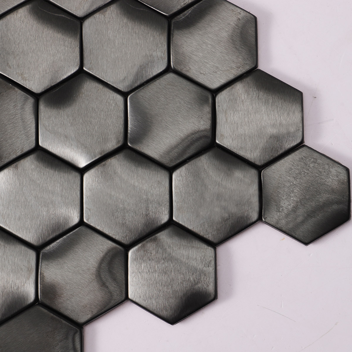 Close-up of wavy 3D metal black brushed stainless steel hexagon mosaic tiles.