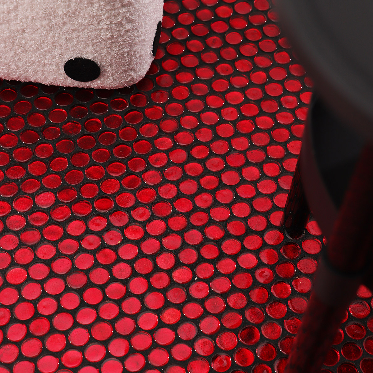 Floor view of red glass circular mosaic tiles with black grout, with a small white stool.