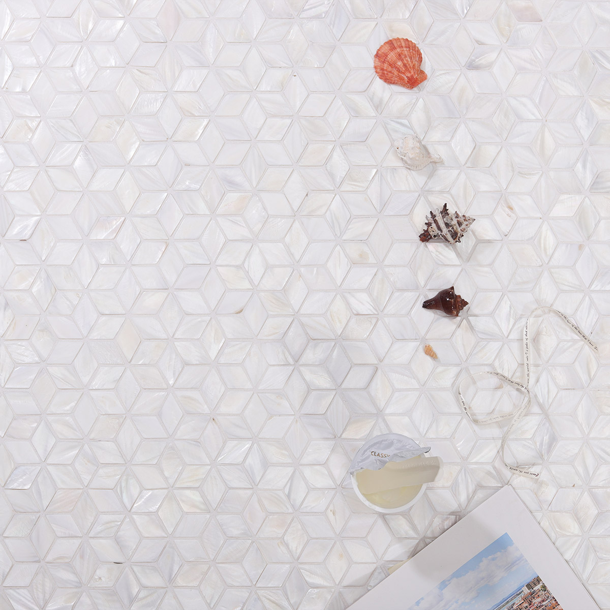 White mother of pearl mosaic tiles in the background with seashells beside them.