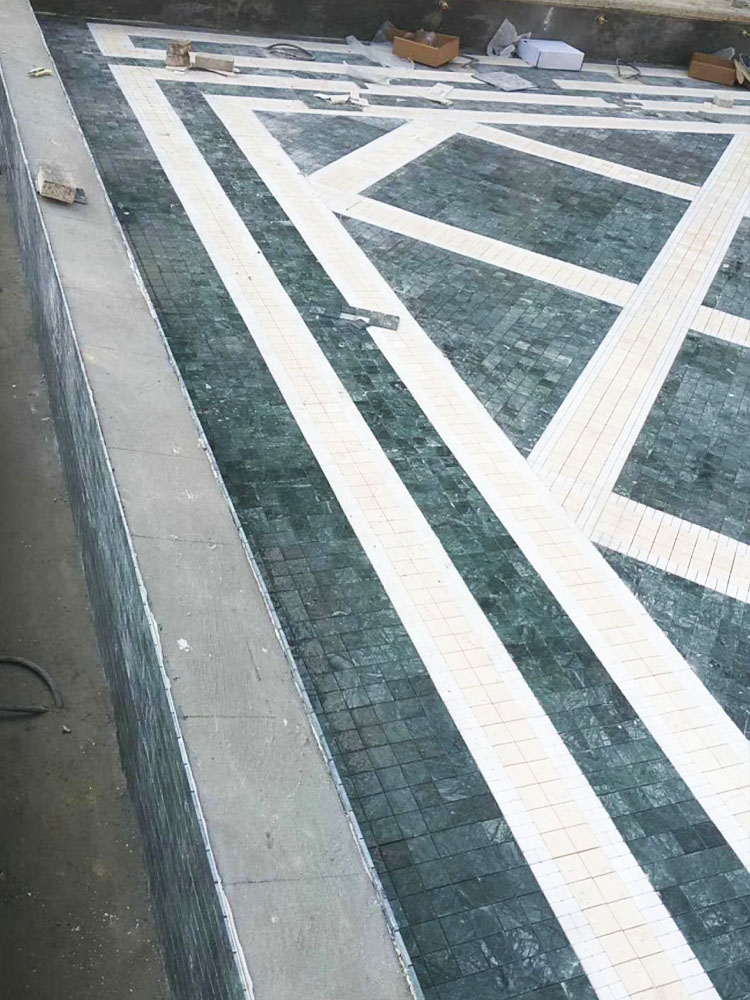Green and beige natural marble mosaic tiles at the swimming pool construction site.