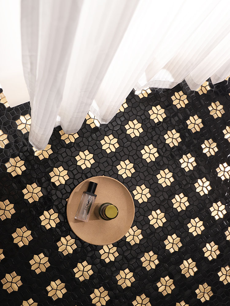 Black background with gold floral mosaic tiles on the floor, next to white curtains.