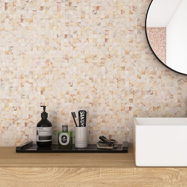 Beige mother of pearl mosaic tiles on the bathroom wall with toiletries and a mirror in front.