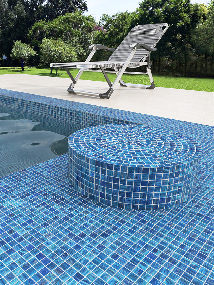 The blue glass mosaic tiles give the swimming pool a sparkling, refreshing look, while the white lounge stool adds a touch of relaxation by the poolside