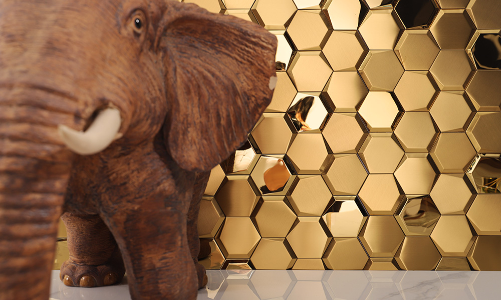 Gold stainless steel hexagon mosaic tiles on the wall with a ceramic elephant in front.