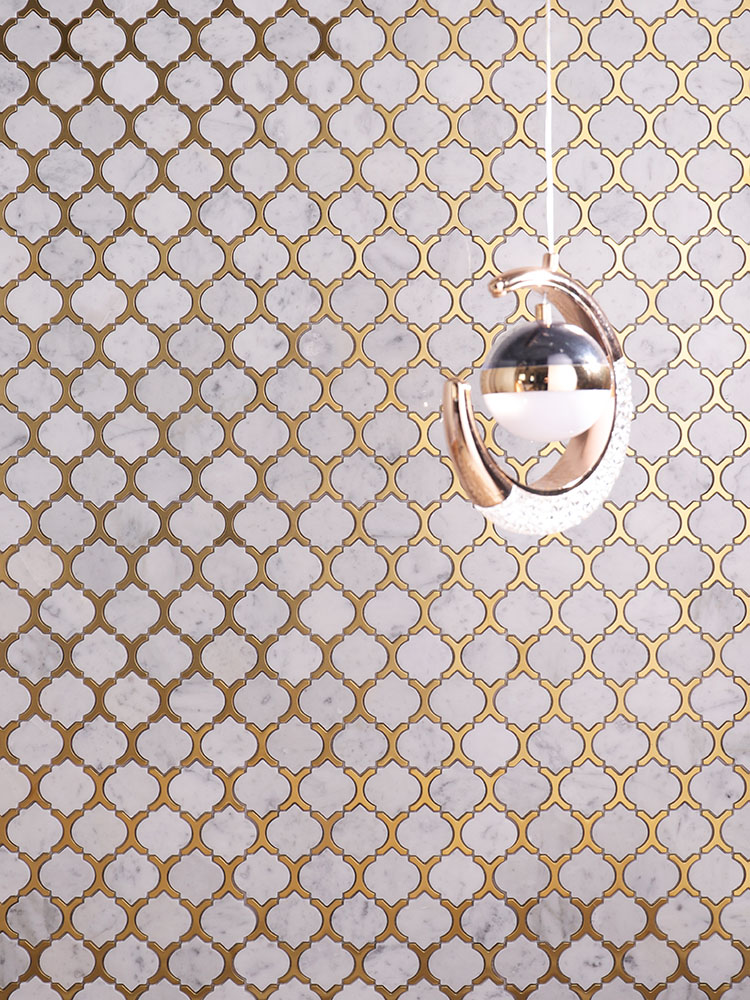 White and gold arabesque marble mosaic tiles on the wall with a chandelier in front.