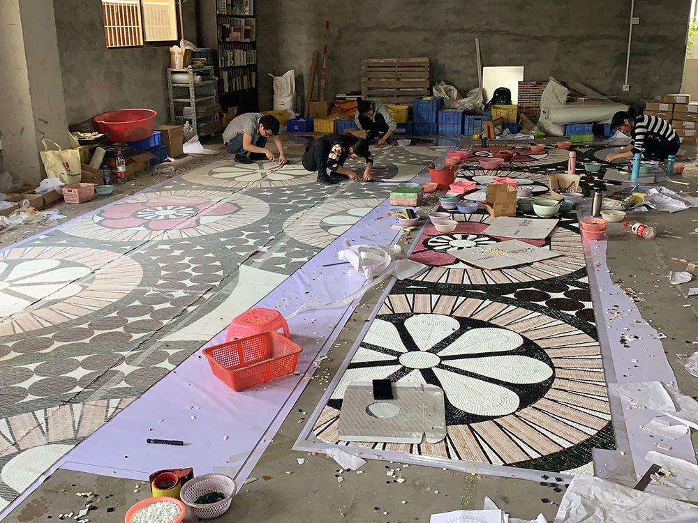 Handcrafting mosaic on the factory floor, workers meticulously arranging tiles into intricate patterns.