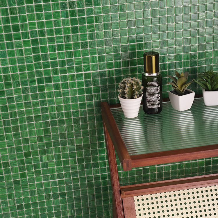 Green mosaic tiles on the wall with a cabinet in front holding small plants and a bottle.