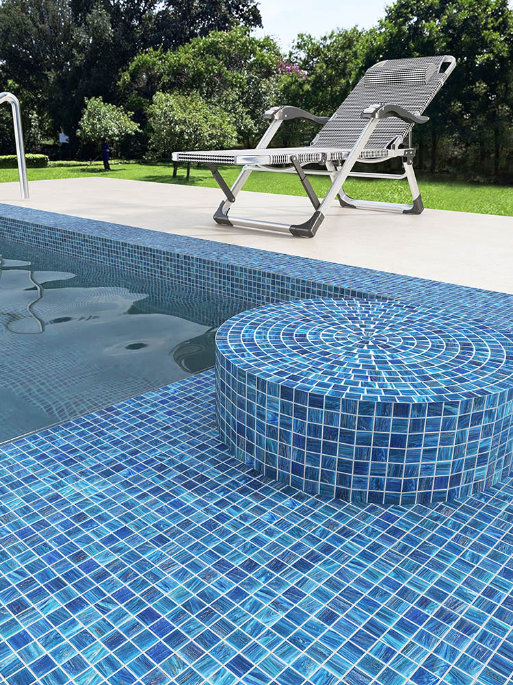 Blue mosaic tiles in the pool with a round pillar covered in mosaic tiles by the poolside.