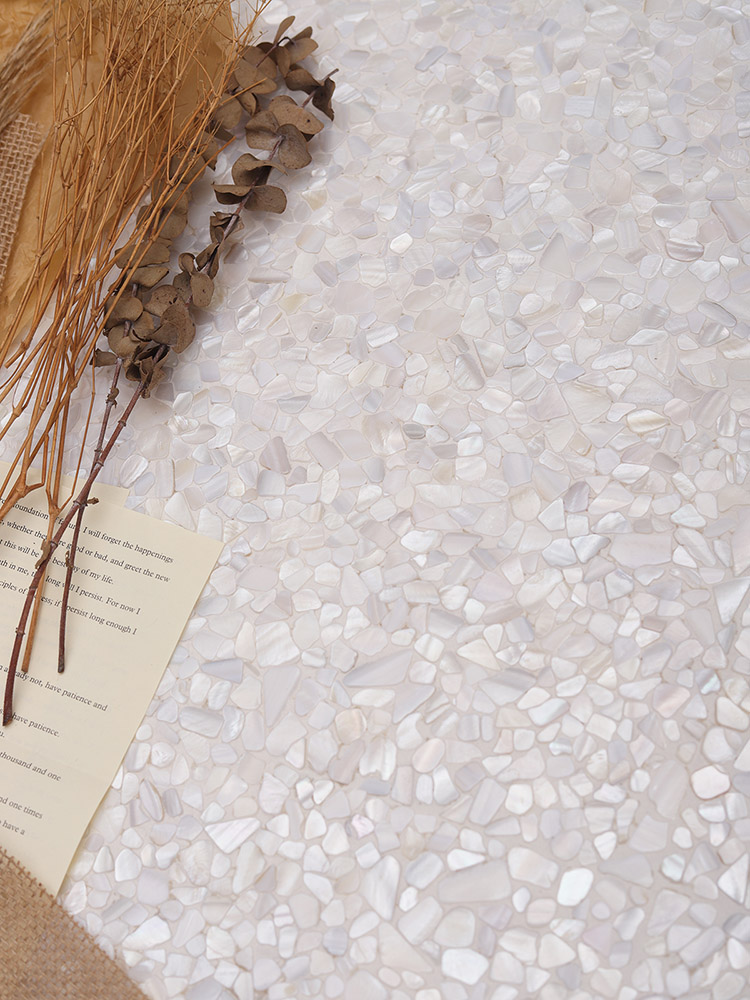 Fragmented and cracked white mother of pearl mosaic tiles with dried branches nearby.