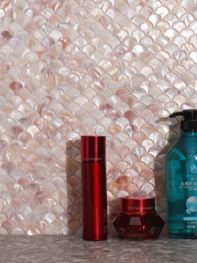 Fan-shaped beige mother of pearl mosaic tiles on the wall with skincare products in front.