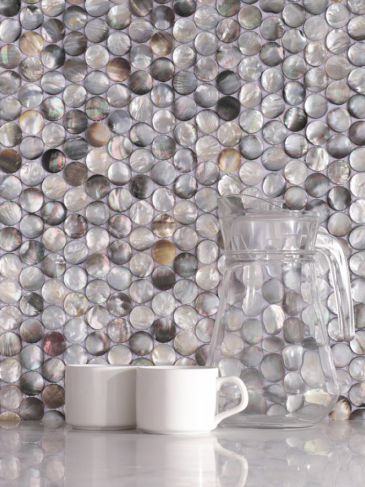 Round black mother of pearl mosaic tiles on the wall with cups and a kettle in front.