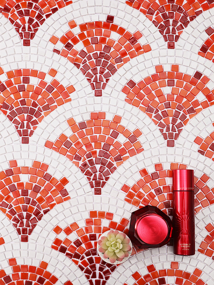 Red and orange handmade fish scale mosaic tiles with a red cosmetics bottle beside them.