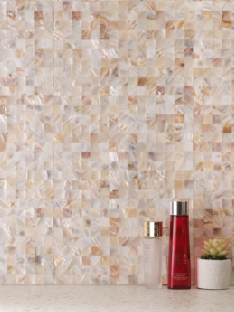 Square beige mother of pearl mosaic tiles on the wall with skincare products in front.