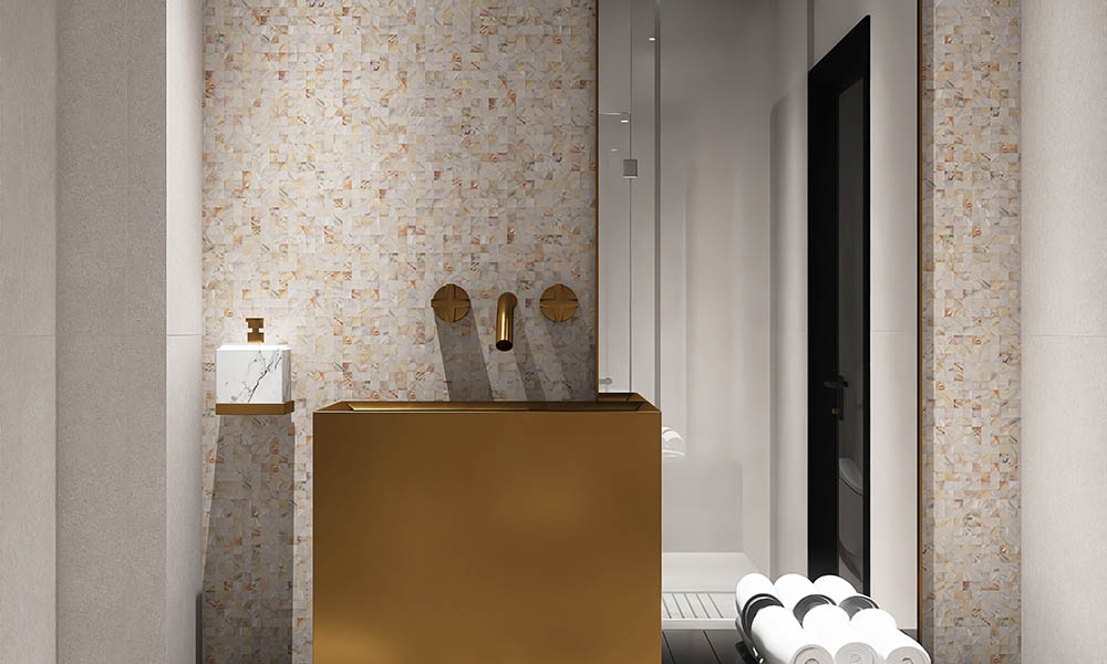 Beige mother of pearl mosaic tiles on the bathroom wall with a gold sink in front.