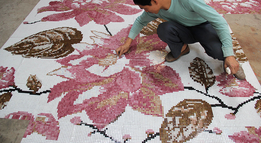 A worker inspecting pixel mosaic tiles being installed on the floor.