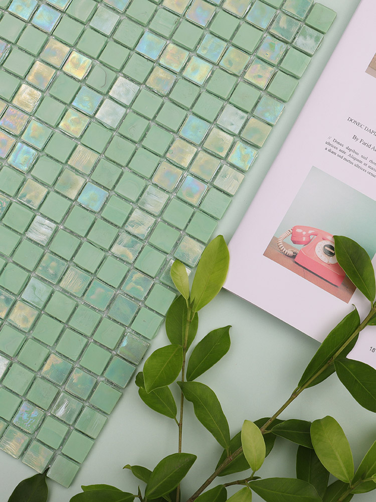 Close-up of green iridescent mosaic tiles with a green leaf nearby.