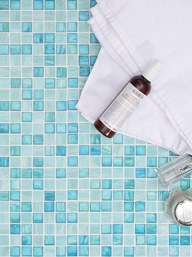 Blue-green glass mosaic tiles with a white towel and skincare products beside them.