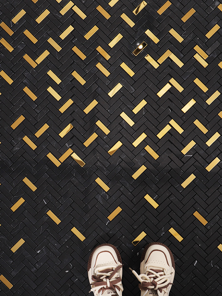 The elegant black marble and gold stainless steel herringbone mosaic pattern enhances the floor with a luxurious and modern design, adding sophistication to the space