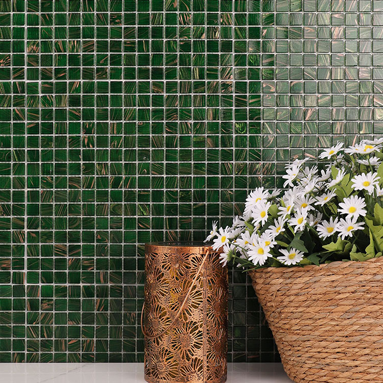 Dark green glass mosaic tiles on the wall with a bouquet of flowers and a vintage lamp in front.