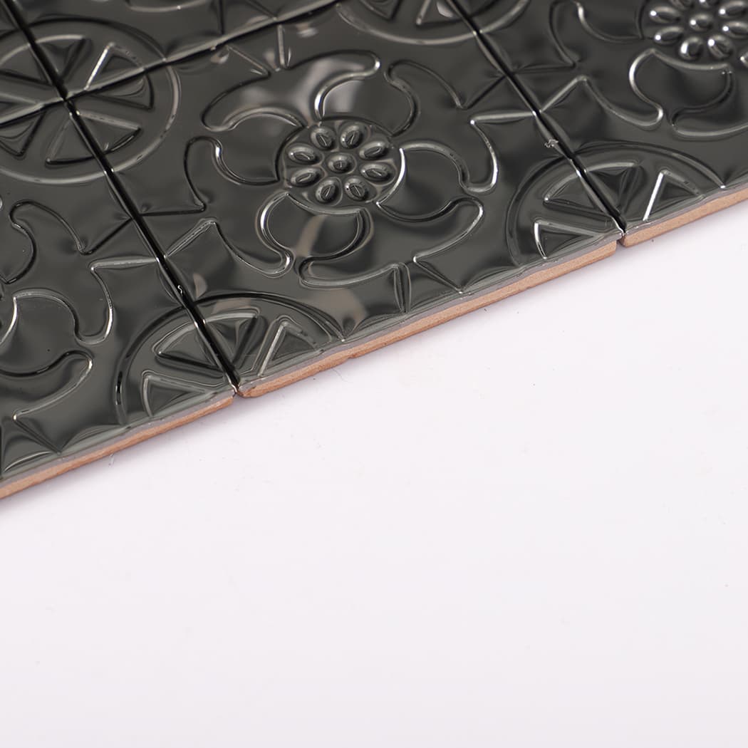 Edge profile close-up showing thickness and emboss depth of black metal mosaic tiles.