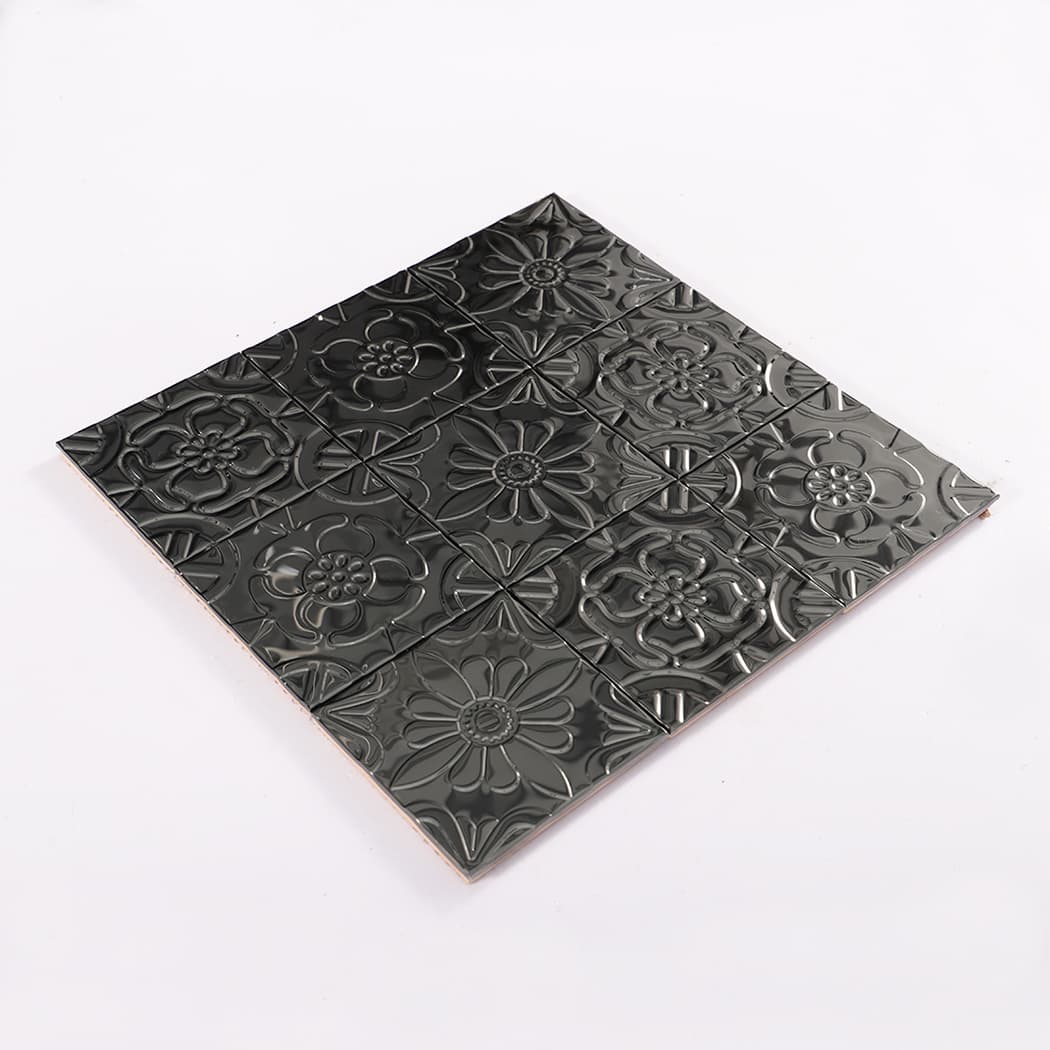 Angled view of a black embossed patchwork mosaic tile sheet on a white background.