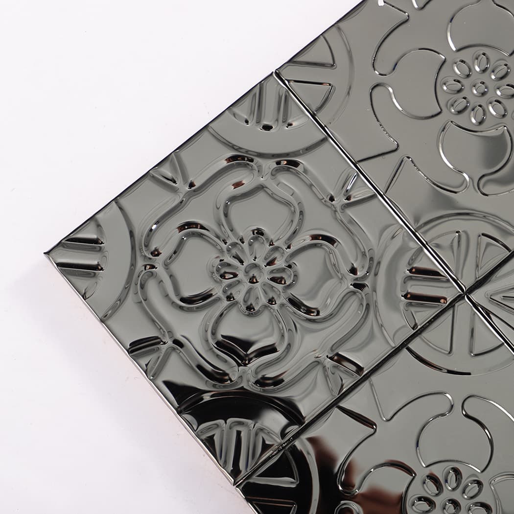 Corner close-up of black embossed metal mosaic tiles showing raised floral detail.