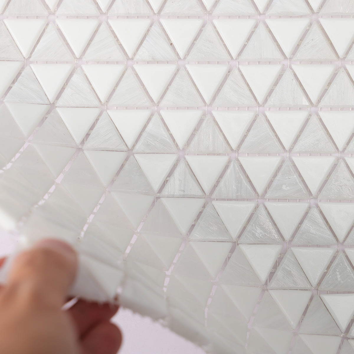 Close-up of white triangular mosaic tile sheet being flexed, showing its flexible mesh backing