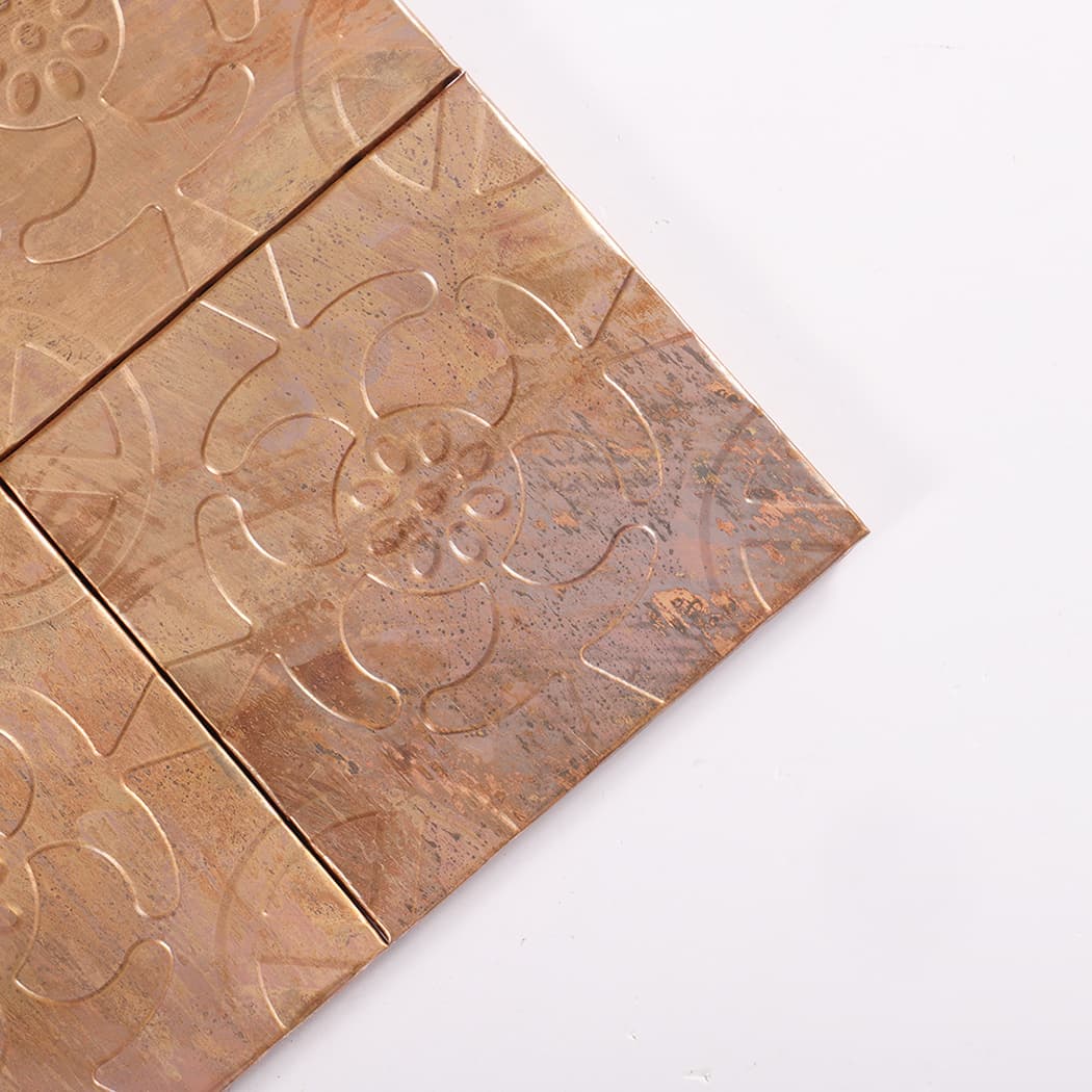 Close up of a copper embossed flower tile corner showing texture and grout lines.