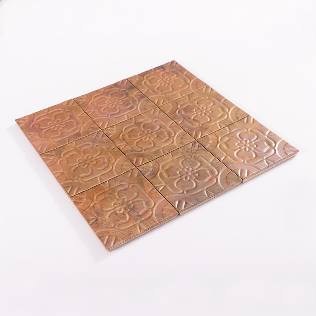 Perspective view of copper embossed four petal flower mosaic tile sheet on a white background.