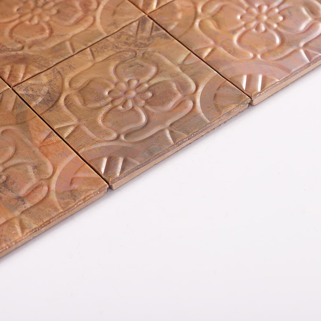 Side angle view of copper embossed flower mosaic tile sheet showing raised pattern and edges.