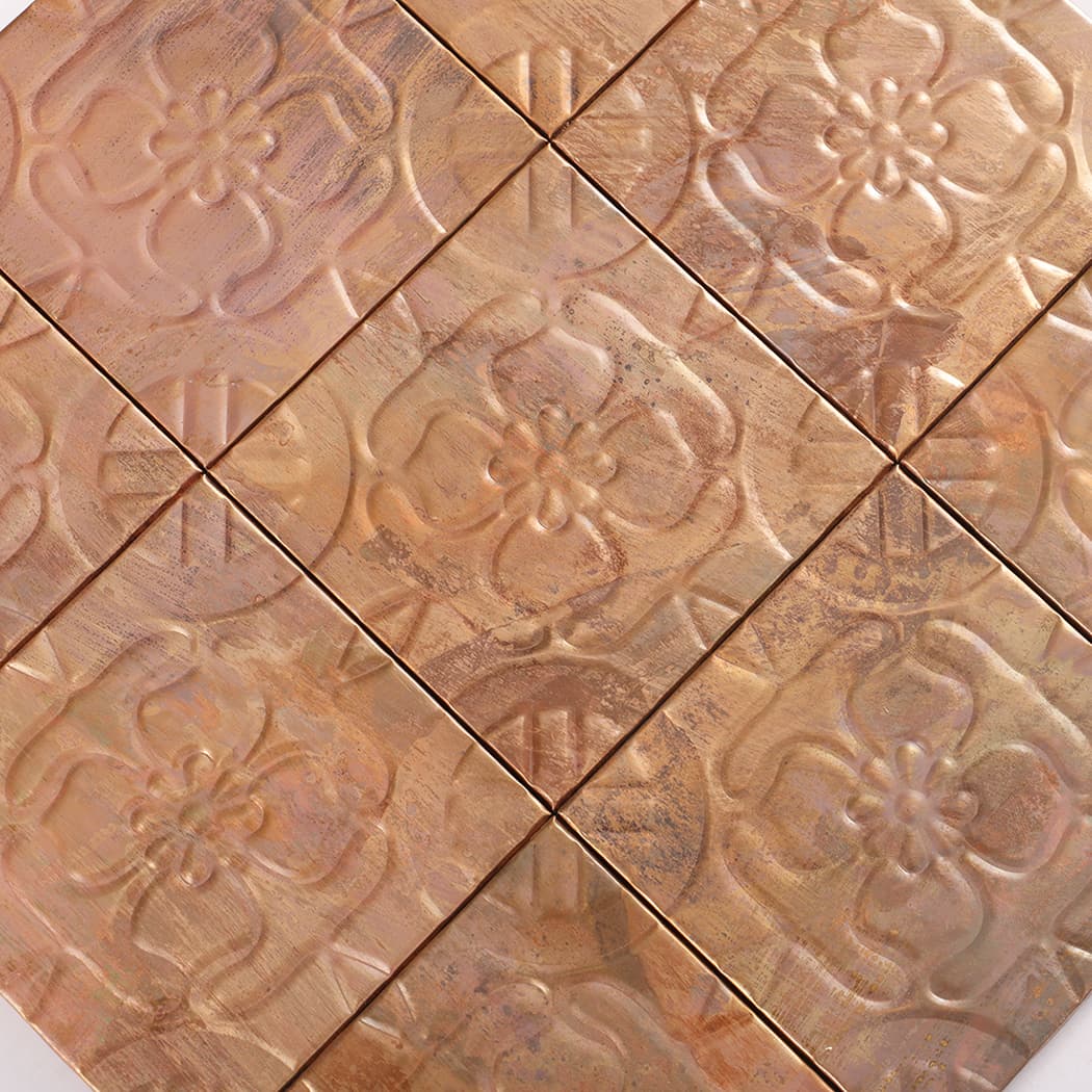Diagonal close up of copper embossed four petal flower tiles with a mottled metallic finish.
