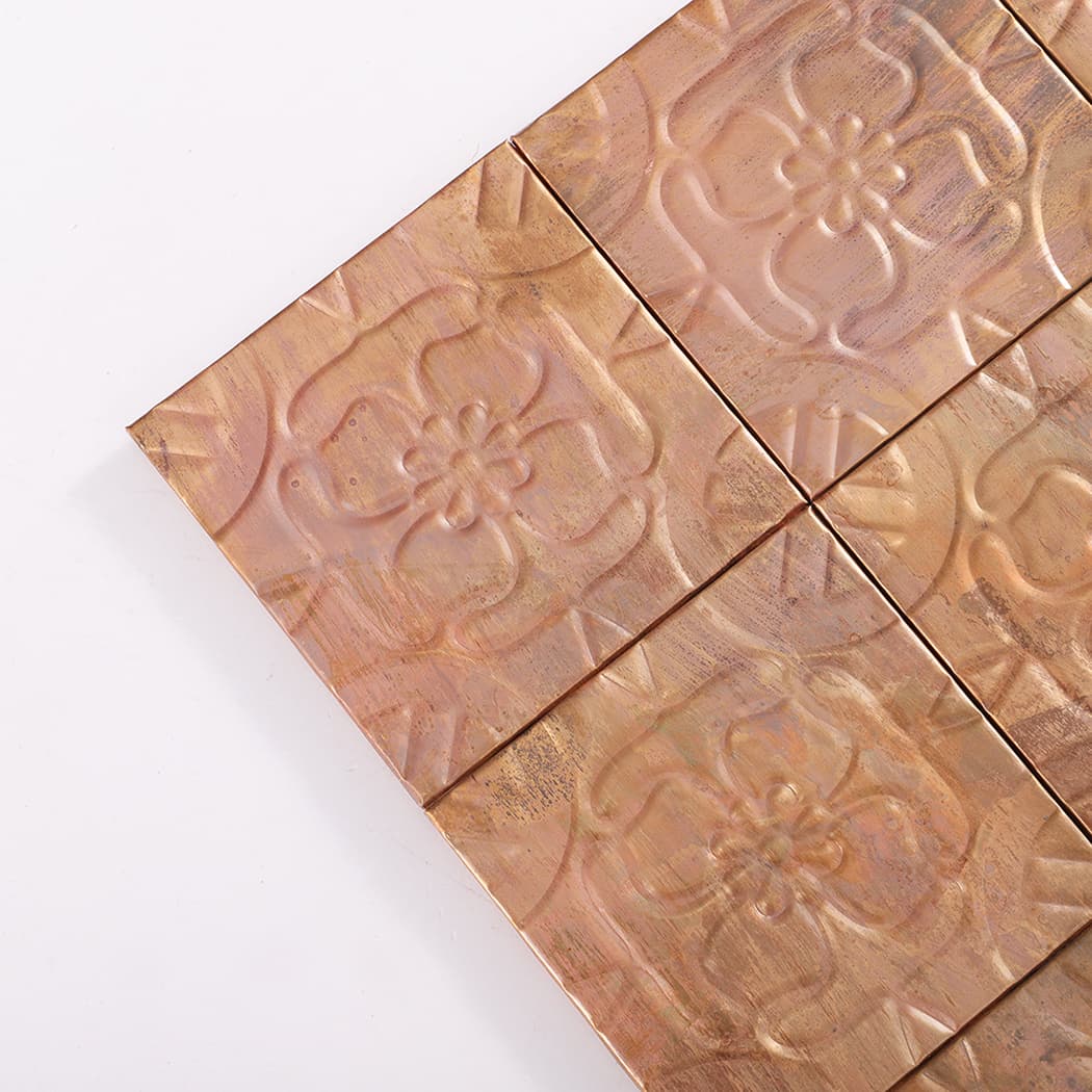 Close up corner of copper four petal flower embossed mosaic tiles showing texture and seams.