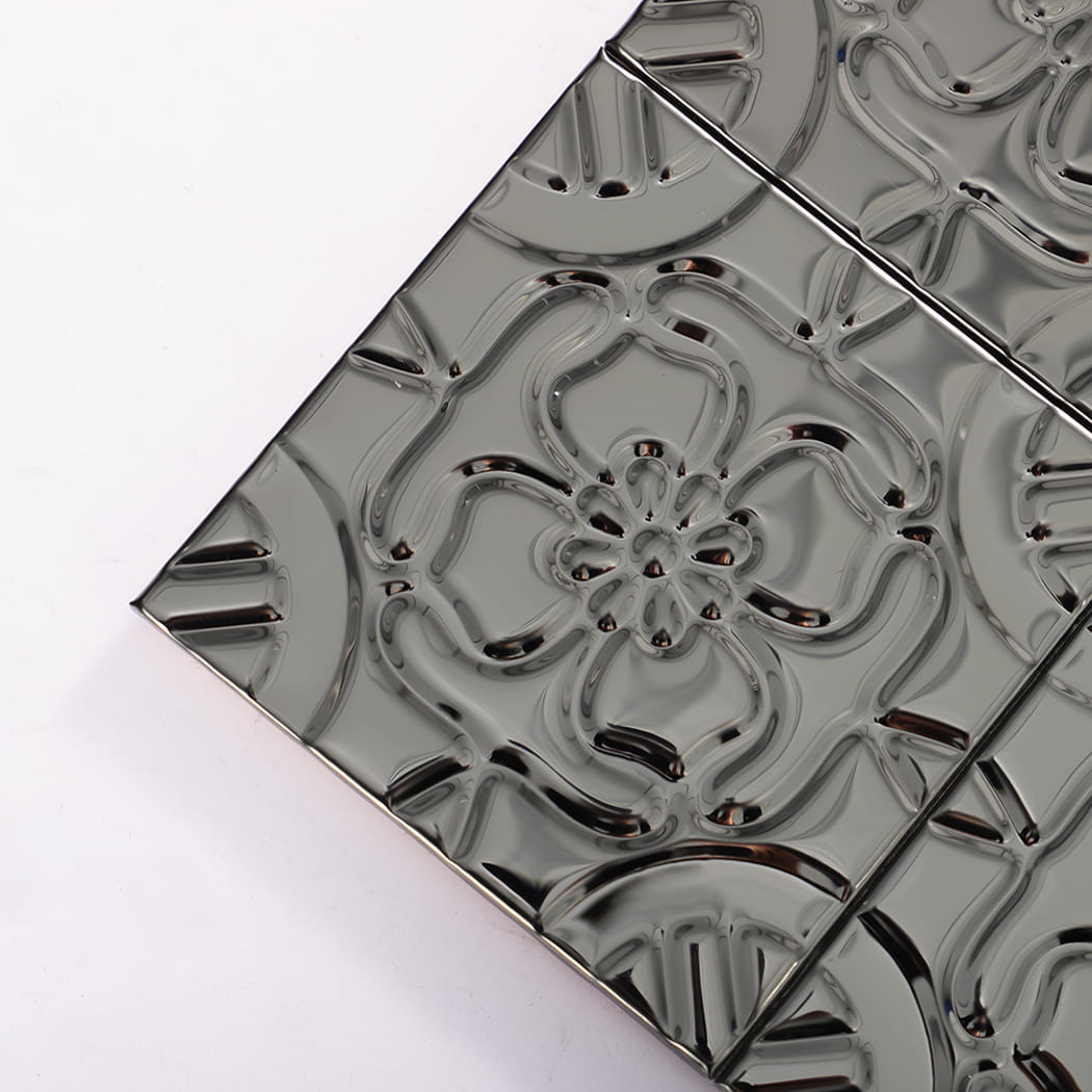Close-up corner of embossed black floral metal tiles with raised pattern and grout lines.