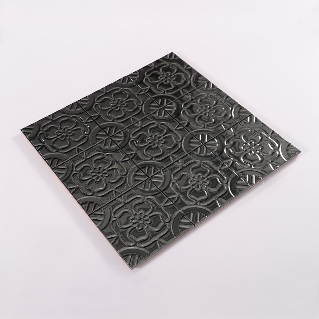 Perspective view of embossed black floral metal wall tile sheet laid on white surface.